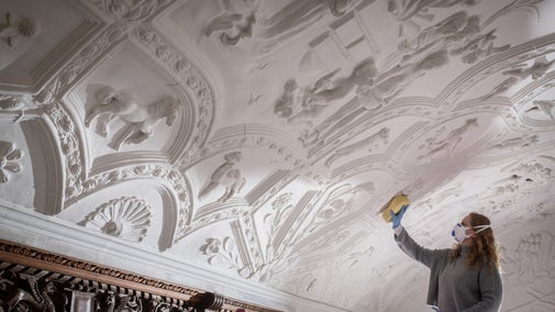 Conservator using a sponge cleaning the Long Gallery ceiling at Lanhydrock